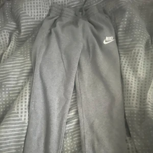 Grå mjukisbyxor från Nike  - Säljer ett par grå mjukisbyxor från Nike i storlek XL men är som 158-170.Byxorna har resår och snörning i midjan, sidofickor och klassisk Nike-logga broderad på låret. Tillverkade i mjukt bomullsmaterial för maximal komfort.