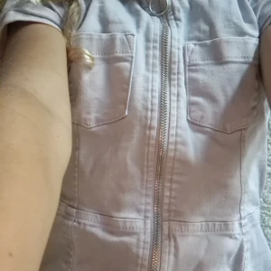 Ljuslila jens klänning från Lindex - Säljer en ljuslila klänning från Lindex med cool dragkedja framtill och två bröstfickor. Klänningen har korta ärmar och är gjord i mjuk bomull, perfekt för dig som gillar enkel och chill stil. Passar dig som vill ha något bekvämt och snyggt.