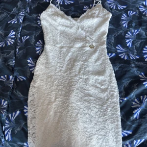 Vit spetsklänning från Chiara Forthi - Supersnygg lång vit spetsklänning från Chiara Forthi med smala axelband och v-ringad hals. Klänningen har en figurnära passform och är helfodrad med mjukt tyg. Spetsen ger en lyxig känsla och en liten guldfärgad logodetalj framtill.