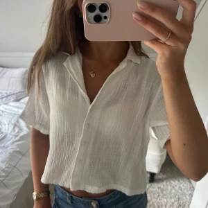 Vit croppad skjorta - Säljer en vit, croppad skjorta i tunn och luftig. Skjortan har korta ärmar, klassisk krage och knappar framtill. Perfekt för varma dagar och ger en chill vibe till jeans eller kjol.