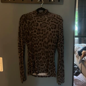 Leopardmönstrad polotopp i grått - Säljer en slim polotopp med leopardmönster i mörkgrå och svart. Toppen har lång ärm och sitter tight mot kroppen, perfekt för dig som vill sticka ut med en edgy look. Materialet är stretchigt och följsamt, vilket gör den superbekväm.