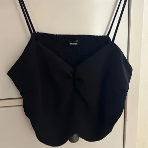 Svart croppad linnetopp Bik Bok - Snygg svart croppad linnetopp från Bik Bok med smala dubbla axelband och twistad detalj framtill. Toppen har smockad rygg för extra komfort och sitter tight över bysten. Perfekt att styla med höga jeans eller kjol.