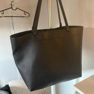 Svart shoppingväska från ONLY - Stor svart shoppingväska från ONLY i stilren design. Väskan är tillverkad i präglat syntetmaterial med två långa handtag och magnetknäppning upptill. Perfekt för dig som vill ha plats för allt du behöver under dagen.