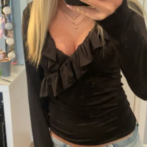 Svart omlottopp med volang från Amisu - Supersnygg svart omlottopp från Amisu med långa ärmar och volangdetaljer längs den v-ringade urringningen. Toppens material är mjukt och stretchigt, perfekt till jeans eller kjol. Säljer då den inte kommer till användning längre!❤️ storleken på tröjan är M men passar mig perfekt som jag xs-S