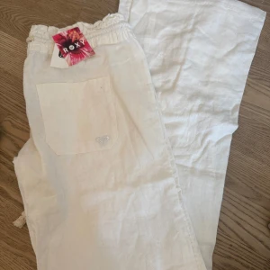 Vita linnebyxor från Roxy XS - Snygga och luftiga vita linnebyxor från Roxy i storlek XS. Byxorna har resår i midjan, 2 bakfickor med brodderat hjärta och lowwaist. Har aldrig anvönts, köpt tidigare iår, lappen sitter kvar och jag har även ett par andra i mörklblå, strl xs om intresse💞