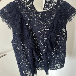Mörkblå spetsblus från Zara - ALDRIG ANVÄND! Säljer en mörkblå blus från Zara med blommigt spetsmönster och korta ärmar. Blusen har en feminin och detaljerad look med transparent spets och fina kanter. Perfekt för dig som gillar att sticka ut med snygga detaljer och elegant vibe.