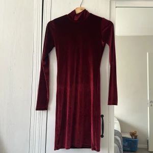 Vinröd sammetklänning från Chiquelle - Säljer en vinröd sammetklänning från Chiquelle i storlek XS. Klänningen har lång ärm, hög krage och är figurnära med kort längd. Baksidan har en liten knappdetalj vid nacken. Perfekt för dig som gillar mjuka material och stilren look.