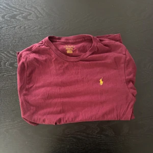 Vinröd t-shirt från Polo Ralph Lauren - Snygg vinröd t-shirt från Polo Ralph Lauren med klassisk gul broderad logga på bröstet, tröjan är i bra skick. Ny pris 1000 mitt pris är 499, men pris kan självklart diskuteras!!! Storlek m men passar även S 