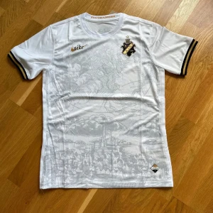 Vit AIK fotbollströja Nike Stockholm - AIK fotbollströja i vitt med subtilt stadsmotiv på framsidan, svarta och gula detaljer på ärmsluten och klubbmärke på bröstet. Tillverkad i lätt och ventilerande material, perfekt för match eller träning. Rund halsringning och klassisk passform.