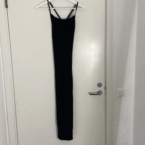 Svart långklänning från SHEIN - Supersnygg svart långklänning från SHEIN med smala axelband som korsas i ryggen. Klänningen är figurnära och har en minimalistisk stil, perfekt för dig som gillar enkel men elegant look. Materialet känns mjukt och följsamt mot kroppen.