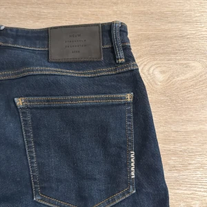 Mörkblå neuw jeans slim - Säljer ett par mörkblå neuw jeans med slim passform. Klassisk femficksmodell med snygga kontrastsömmar och läderpatch bak i midjan. Jeansen är tillverkade i stretchig denim för extra komfort och sitter tajt längs benen. Passar mig perfekt, jag är 185cm och väger 75kg👌
