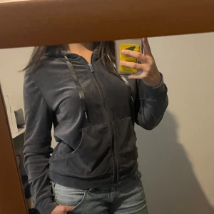 Mörkgrå hoodie med dragkedja - Säljer en mörkgrå hoodie med dragkedja och huva. Tröjan har snörning vid huvan, två stora fickor framtill och ribbade muddar vid ärmslut och nederkant. Mjuk och skön. 