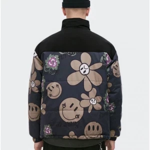 Earth Song pufferjacka med blommor - Fet pufferjacka från Earth Song med svart axelparti och färgglatt blommönster i beige, lila och grönt. Jackan har dragkedja framtill, hög krage och coola smiley- och blomdetaljer över hela tyget. Perfekt statement-piece för dig som vill sticka ut.