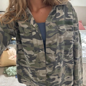 Camouflage overshirt från Pull&Bear - Säljer en oversized camouflagefärgad overshirt från Pull&Bear. Jackan har klassisk krage, knäppning framtill, två bröstfickor med lock och långa ärmar. Tillverkad i bomull, perfekt för lager-på-lager och streetstyle.