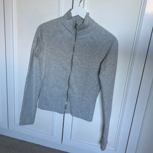 Grå ziptröja från Nelly - Säljer en stilren grå ziptröja från Nelly i storlek S. Tröjan har hög krage, hel dragkedja framtill och är tillverkad i mjuk bomullsblandning. Perfekt för lager-på-lager och chill dagar. Långärmad och enkel att matcha med det mesta.
