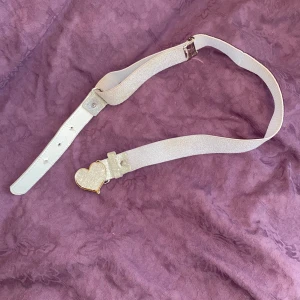 Skärp Y2K - Supersnyggt vitt bälte med glittrig yta och ett hjärtformat spänne i silver. Bältet har en elastisk del och justerbara hål. Ca 80 cm långt!