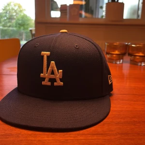 Blå LA Dodgers keps från New Era (Helt Ny) - Snygg blå New Era 59FIFTY keps med LA Dodgers broderat i vitt framtill och MLB-logga baktill. Säljer för att jag köpte fel storlek så den är helt oanvänd. Klassisk flat brim och broderad New Era-logga på sidan. Tillverkad i polyester, perfekt för dig som gillar sportig stil och baseball.