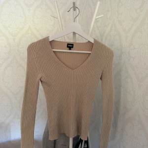 Beige ribbad tröja från RYVLS - Säljer en beige ribbad tröja från RYVLS med v-ringning och lång ärm. Tröjan har en slim passform och är perfekt för dig som gillar en enkel men snygg stil. Materialet är mjukt och stretchigt, vilket gör den riktigt skön att ha på sig.