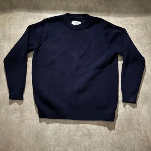 Mörkblå stickad tröja från Maison Margiela - Säljer en mörkblå stickad tröja från Maison Margiela. Tröjan har klassisk rund halsringning, ribbade muddar och är långärmad. Perfekt för dig som gillar minimalistisk och stilren design med lyxig känsla. Hör av vid minsta fundering 💫