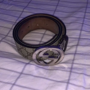 Gucci bälte - Säljer ett klassiskt Gucci GG Supreme bälte med ikoniskt GG-mönster och stor silverfärgad logospänne. Bältet är i brunt och beige skinn med tryckt monogram och insida i ljust brunt läder. Perfekt accessoar för att lyfta vilken outfit som helst.