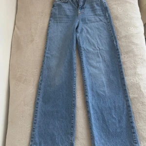 Blå wide jeans  - Säljer ett par ljusblå jeans i storlek 32. Modellen har raka, vida ben och klassisk femficksdesign. Jeansen har dragkedja och knapp framtill samt snygga kontrastsömmar. Perfekta för en chill och trendig look.