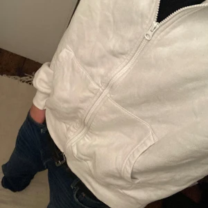 Vit hoodie med dragkedja från Lindex - Vit hoodie från Lindex i storlek 170. Tröjan har huva, dragkedja framtill och två fickor. Tillverkad i mjuk bomullsmix, perfekt för chill dagar. Klassisk passform och långärmad modell. Pris ej hugget i sten 