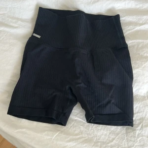 Svarta ribbade cykelshorts från Aim'n - Svarta cykelshorts från Aim'n med hög midja och ribbad struktur. Stretchigt material som sitter skönt och följer kroppen. Perfekta för träning eller chill, med stilren look och diskret logga vid midjan. Passformen är normal och materialet känns mjukt mot huden.