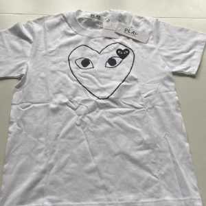 Vit Comme des Garçons Play t-shirt S - Vit t-shirt från Comme des Garçons Play med klassiskt hjärta med ögon-tryck i svart på bröstet och liten svart hjärtdetalj. T-shirten har rund hals, korta ärmar och är gjord i mjuk bomull. Perfekt för dig som gillar streetstyle och ikoniska prints.