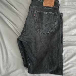 Levi's 501 svarta jeans W33 L32 - Klassiska svarta Levi's 501 jeans med rak passform och knappgylf. Jeansen har fem fickor, tydliga sömmar och den ikoniska läderpatchen bak i midjan. Perfekta för dig som gillar en tidlös och avslappnad stil.