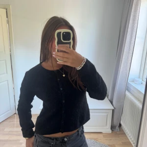 Svart stickad tröja  - Svart stickad kofta med rund halsringning och knäppning framtill. Långärmad och lite loose fit, perfekt att slänga över ett linne eller t-shirt. Enkel och stilren design som funkar till det mesta.