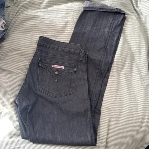Mörkgrå jeans från Hudson, stl 31 - Snygga mörkgrå jeans från Hudson med klassisk femficksdesign och cool detalj på bakfickan. Jeansen är tillverkade i en mix av bomull, nylon och lycra för en skön stretchig känsla. 
