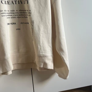 Vit  sweatshirt med tryck från Kappahl - Säljer en vit sweatshirt från Kappahl i storlek XS. Tröjan har ett coolt svart tryck med texten 'CREATIVITY', New York och Art scene 1992 framtill. Mjuk bomullskvalitet, rund hals och långa ärmar med ribbade muddar. Perfekt för dig som gillar streetstyle och grafiska prints.