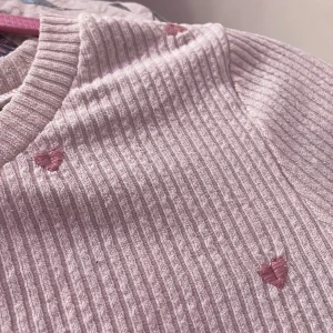 Rosa ribbad tröja med hjärtan - Söt rosa ribbad tröja med små hjärtan i en ljusare nyans. Tröjan är croppad och har långa ärmar, perfekt för en avslappnad stil. Den är både bekväm och stilren, vilket gör den till ett mångsidigt tillskott i garderoben.