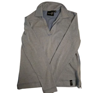 Blå pikétröja från Pelle P - Säljer en stilren blå pikétröja från Pelle P. Tröjan har en klassisk krage och långa ärmar, perfekt för en avslappnad men ändå snygg look. Den är tillverkad i ett bekvämt material och har en diskret logga på baksidan. Notera att färgerna syns lite svagare på bild 1 och 2 pga ljussättning, lappen är även trasig därav lågt pris 