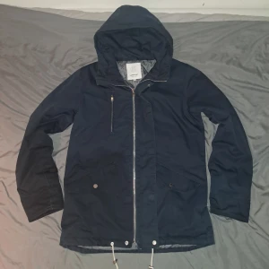 Marinblå jacka från Elvine - Säljer en snygg marinblå jacka från Elvine med huva och dragkedja. Jackan har en quiltad insida och praktiska fickor med knappar. Perfekt för kyligare dagar. Den är nästan aldrig använd.