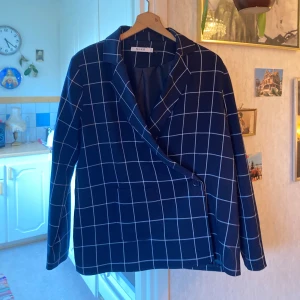 Mörkblå rutig kavaj från NA-KD - Snygg mörkblå kavaj från NA-KD med vitt rutmönster. Kavajen har en elegant omlott-design och långa ärmar. Knappt använd 🌷