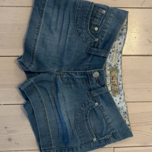 Lågmidjade jeansshorts  - Snygga blå lågmidjade jeansshorts! De har en klassisk femficksdesign och knappar både fram och på bakfickorna. Perfekta för en avslappnad sommarlook. Säljer då de tyvärr var för små för mig. Mått: 38 cm & 26 cm på längden.