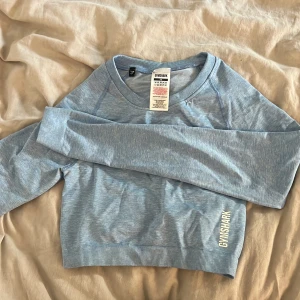 Blå croppad tröja från Gymshark - Säljer en snygg blå croppad tröja från Gymshark. Tröjan har långa ärmar och en en fin detalj i ryggen. Den är i ny skick, storlek XS