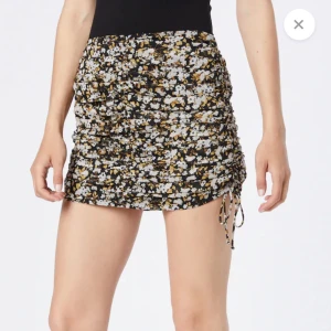 Blommig kortkjol med snörning - Snygg kortkjol med blommigt mönster i svart, vit och gul. Kjolen har en åtsittande passform och snörningsdetaljer på sidorna för en justerbar look. Perfekt för att ge en somrig touch till din outfit! Nypris: 350kr.