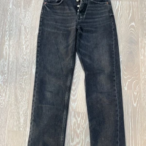 Svarta jeansbyxor från Zara - Snygga svarta jeansbyxor från Zara med hög midja och knappar framtill. Byxorna har en straight passform och är perfekta för en stilren look. Tillverkade i ett slitstarkt denimtyg.