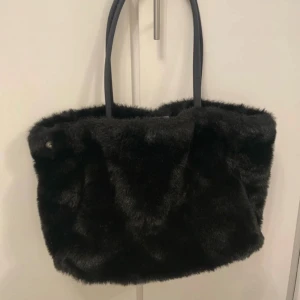 Svart pälsväska - Inte äkta päls*   En svart hoboväska . Finns 2 knappar utanför väskan så att man kan vika in väskan. 