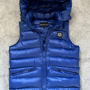 Bvaldi väst - Snygg blå väst från bvaldi med dragkedja och huva.Västen har praktiska fickor med dragkedjor och en stilren design. Ser ut som helt ny, inga defekter! Pris kan sänks vid snabb affär!!!