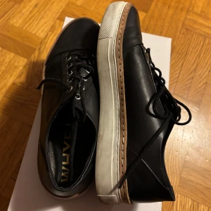 Whyred Beeton - Snygga svarta sneakers i skinn med snörning och vit sula. Perfekta för en stilren look. Har använts en del gånger men fortfarande fint skick.