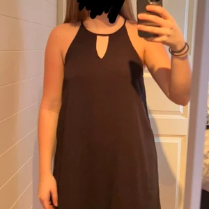 Svart ärmlös klänning - Snygg svart ärmlös klänning med en stilren design och en liten öppning vid halsen. Perfekt för en elegant look.