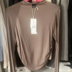 Brun långärmad topp  - Brun långärmad topp från Gina Tricot. Toppen har en mjuk och skön känsla med en lätt rynkad detalj på sidan. 🫶🏼🫧