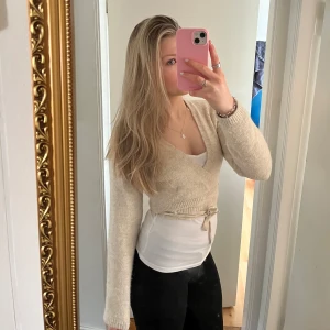 Beige omlottkofta, Bolero - Säljer en mysig beige omlottkofta (bolero)med knytband i midjan. Koftan har långa ärmar och har ett långt band som går att knyta på olika sätt, så som du vill ha det💕