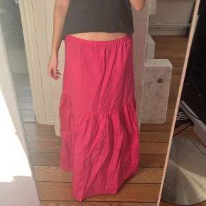 Rosa långkjol - Säljer en härlig rosa långkjol med volangdetaljer. Kjolen har en lös passform och är perfekt för sommarens varma dagar. Den är gjord i ett lätt och luftigt material som ger en skön känsla.