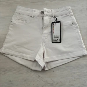 Vita shorts från F2 - Snygga vita shorts från F2 med hög midja och klassisk femficksdesign. Perfekta för sommardagar med en stilren look. De har en knapp och dragkedja framtill för enkel påklädning.