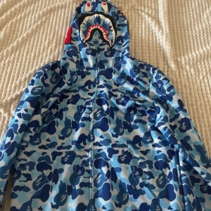 Bape Hoodie - Bape Hoodie 2XL - Passar L/XL - Blå  Säljer en snygg Bape-hoodie i storlek 2XL, men den passar bättre för L eller XL. Färgen är blå, och den har bara använts 3-4 gånger, så den är i mycket bra skick. Anledningen till försäljningen är att den inte kommer till användning.  Perfekt för dig som vill ha en stilren och bekväm hoodie från ett populärt märke!  Hör av dig vid intresse.