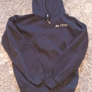 Marinblå  hoodie från Gina Tricot - Säljer en marinblå hoodie från Gina Tricot med texten 'MA CHÉRIE' och hjärtmotiv på  baksidan. Tröjan har en klassisk huva och långa ärmar, perfekt för en avslappnad stil. 🖤